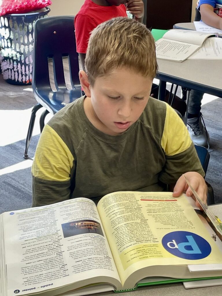 Student focused on independent reading, demonstrating Delphi Academy's Study Technology approach with a textbook in the classroom setting